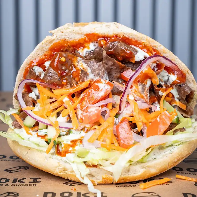 Kebab w bułce z mięsem, warzywami i sosami na tle blachy